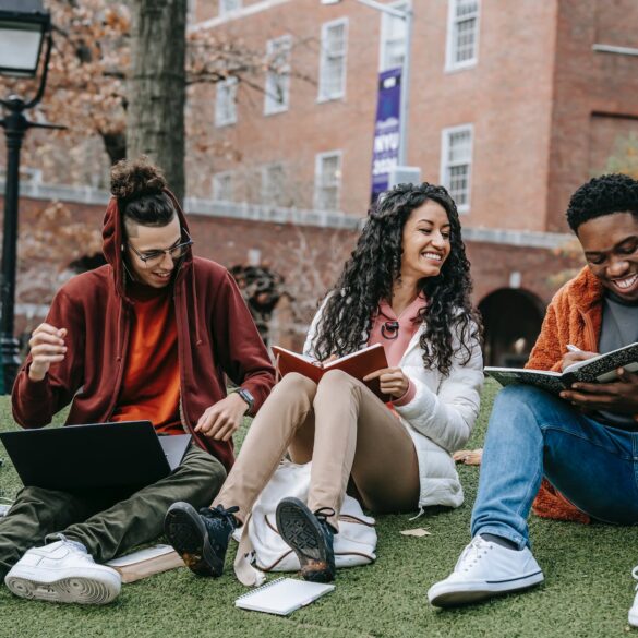 cheerful multiethnic students with books sitting near university