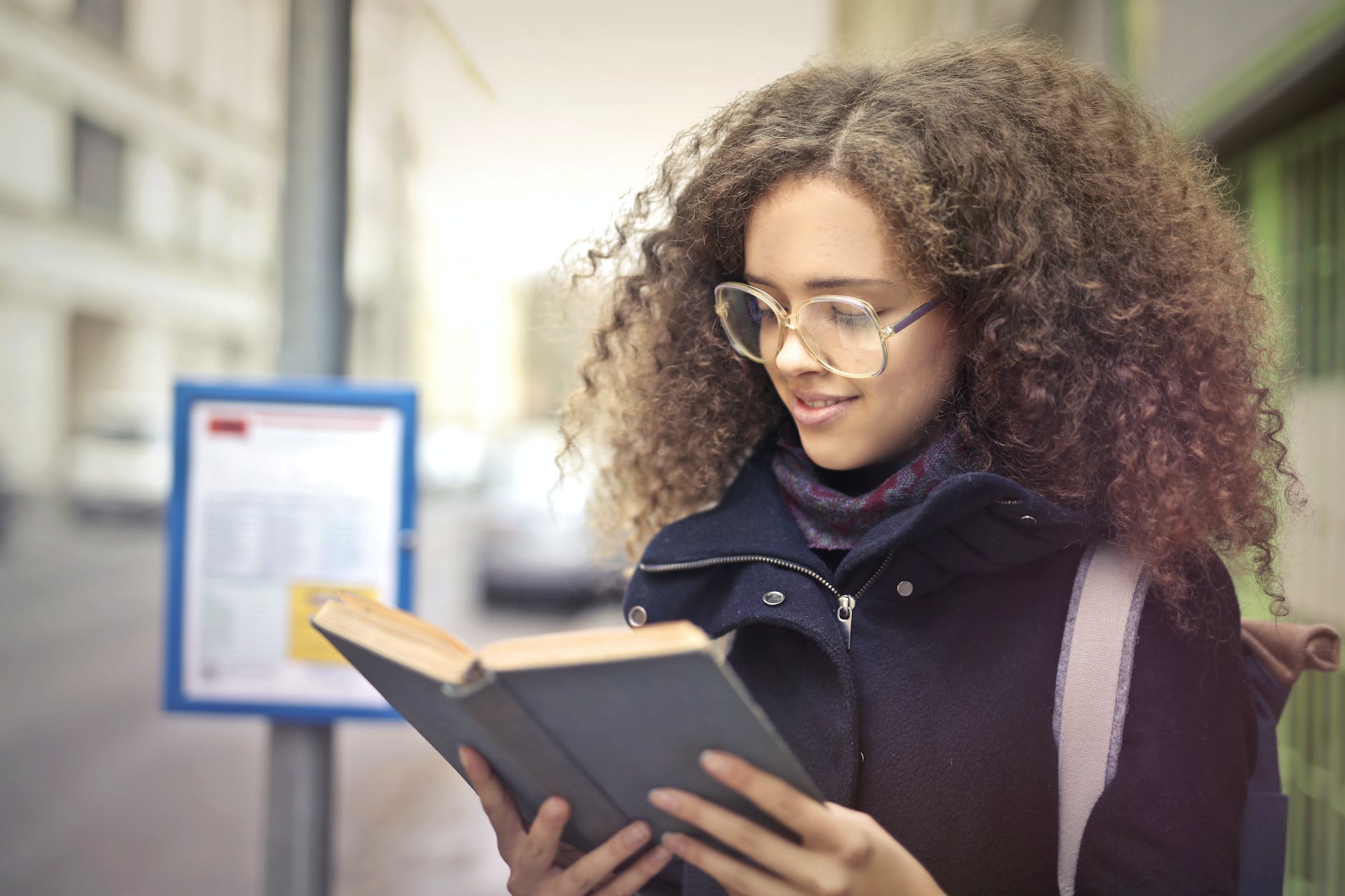 woman with curly hair wearing eyeglasses reading book