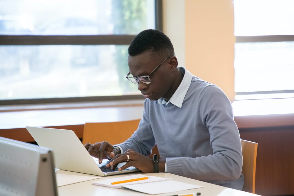 serious young black man working on laptop sitting near window in library