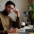 man in brown sweater sitting infront of laptop