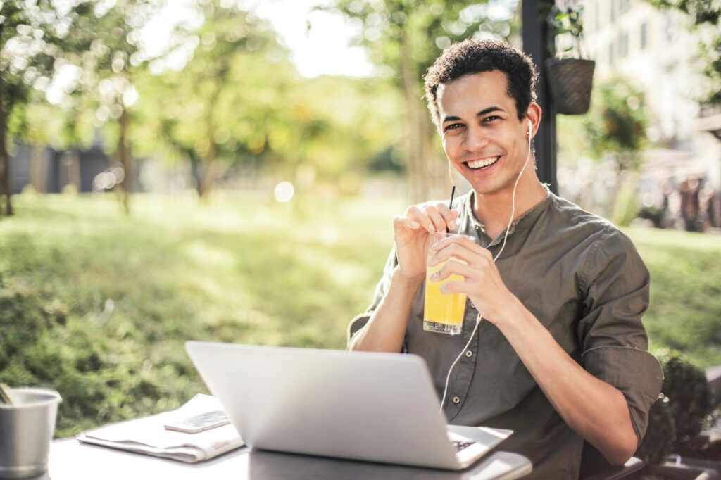 happy man sitting with laptop and juice in park