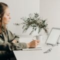 woman in gray coat using white laptop computer